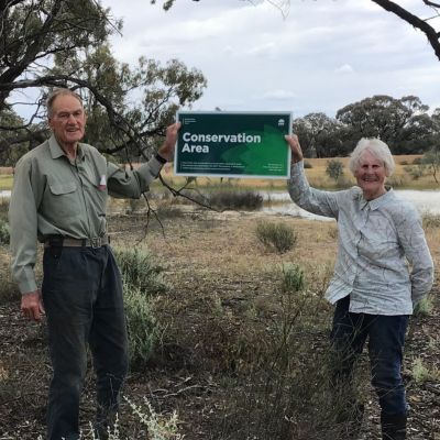 man and woman stand outside holding a conservation sign