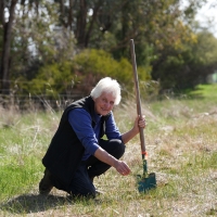 A woman outside posing with a shovel in the ground