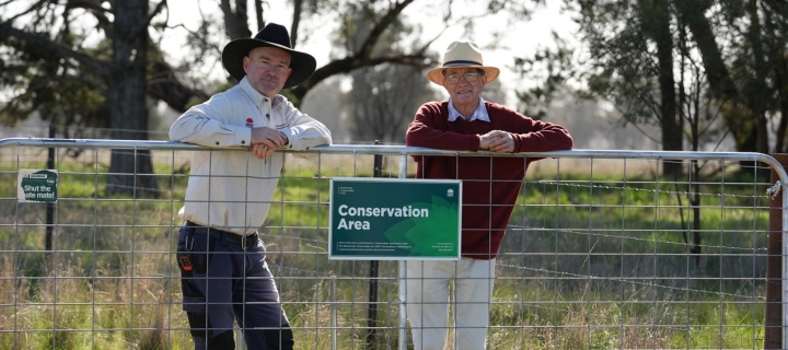 Two men standing behind a gate with a conservation agreement sign attached