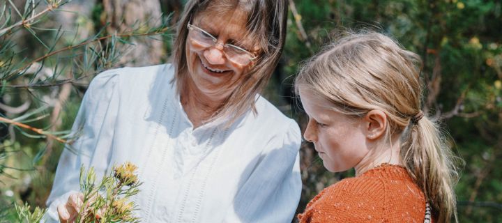 A woman and a younger girl both examining at a tree while outside