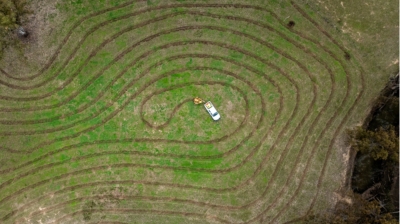 A top down drone shot of a white ute in a grass field