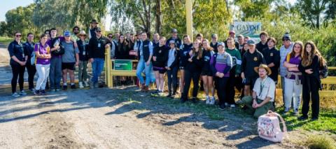 A group of high school aged students stand with educators at the gate to the Gayini property 