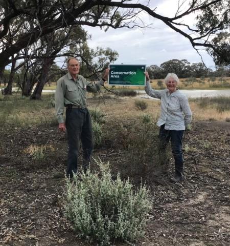 man and woman stand outside holding a conservation sign